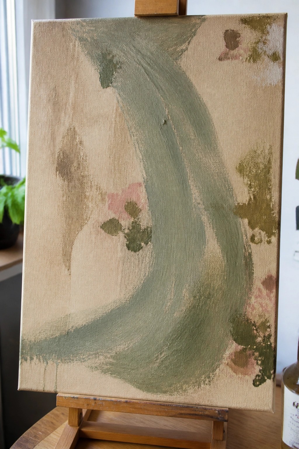 Abstract canvas on wooden easel with green curves, pink flowers, and beige tones