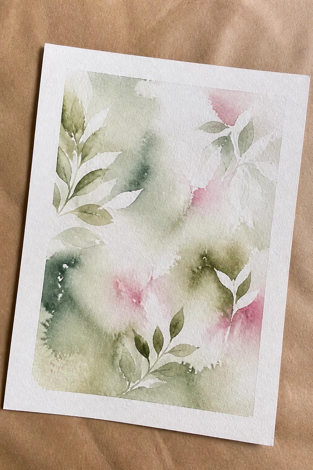 Watercolor painting of green leafy branches with soft pink and green washes on paper