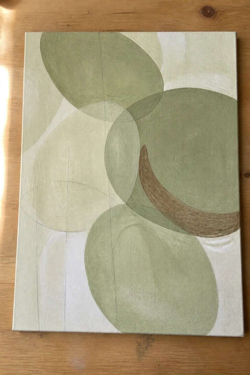 Abstract painting of overlapping green circles and ovals on canvas atop wood.
