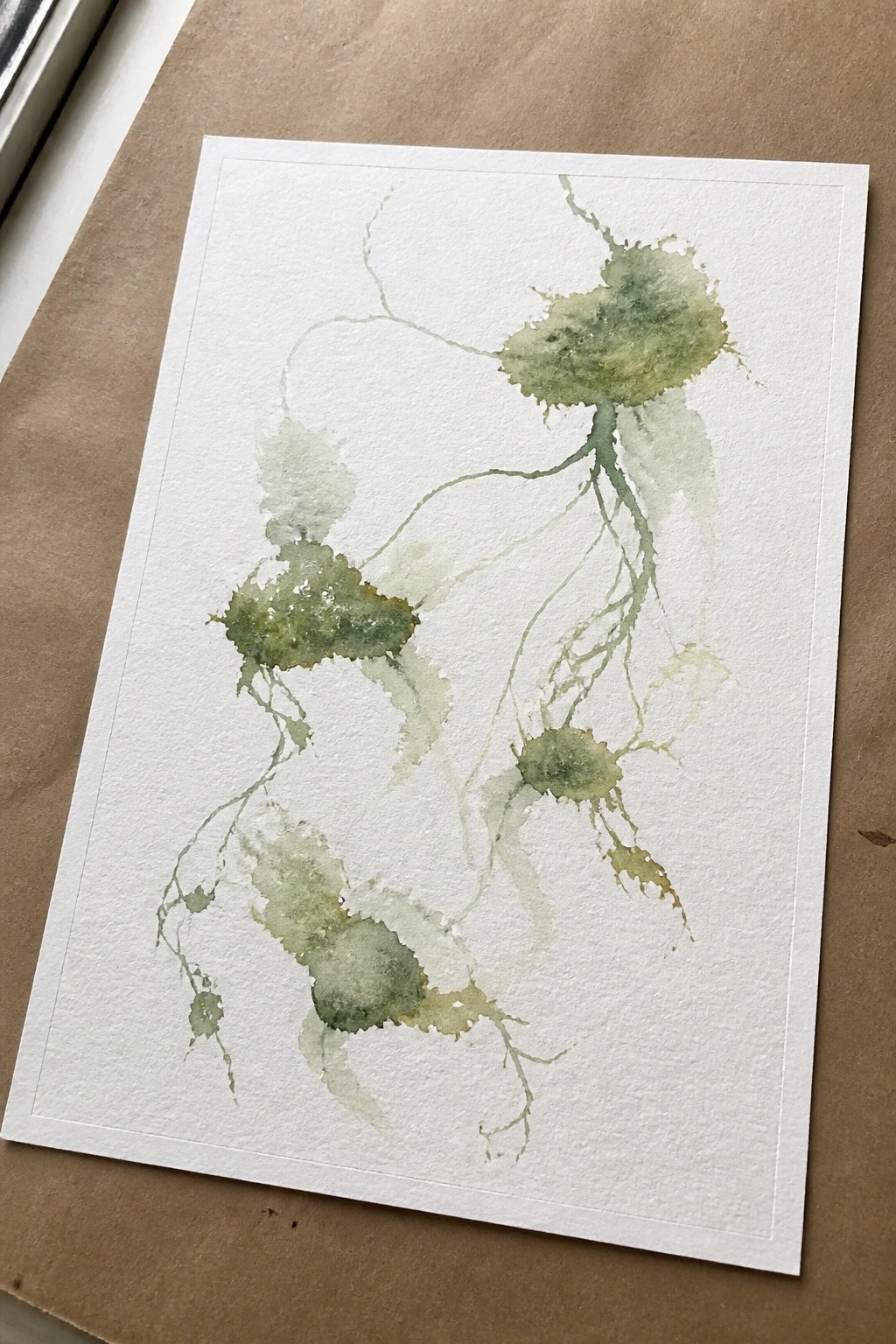 Green watercolor abstract shapes with branching lines on white paper over brown surface