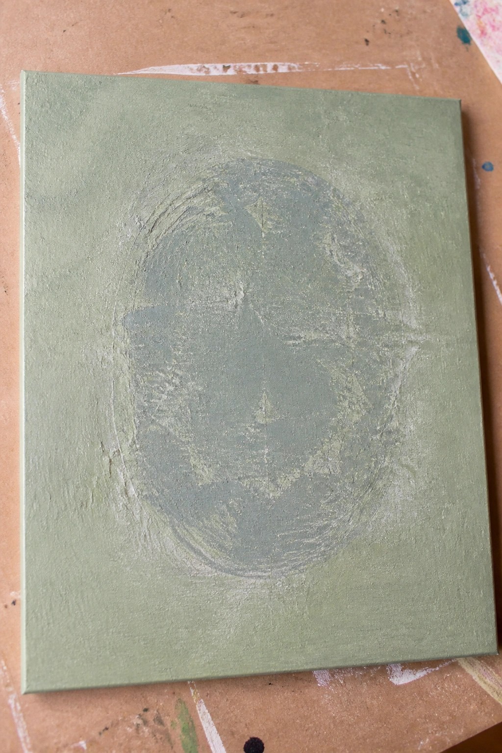 Green canvas with textured darker circular brushstrokes on paint-splattered surface