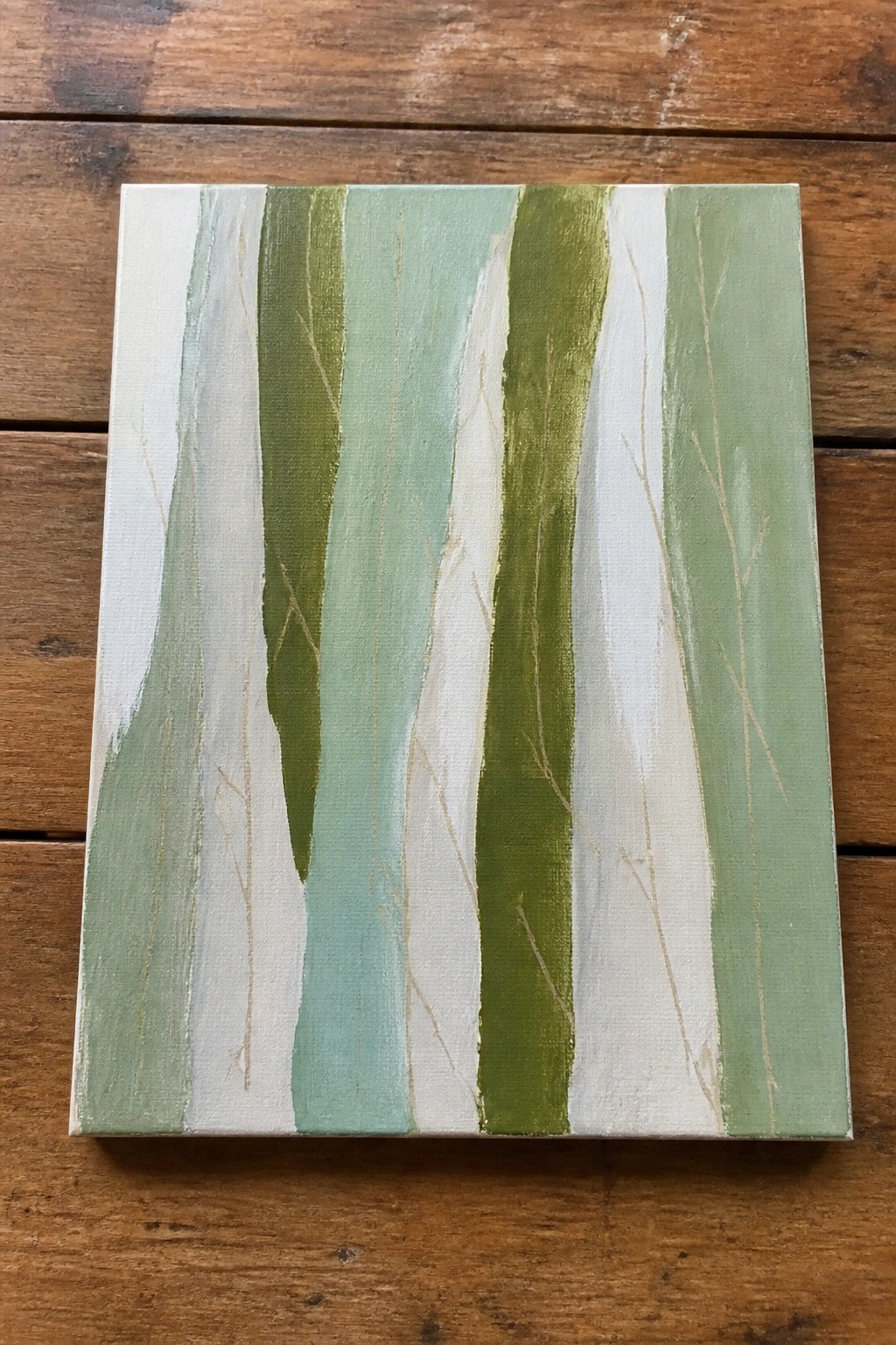 Abstract painting with vertical green-white stripes and gold lines on wooden table