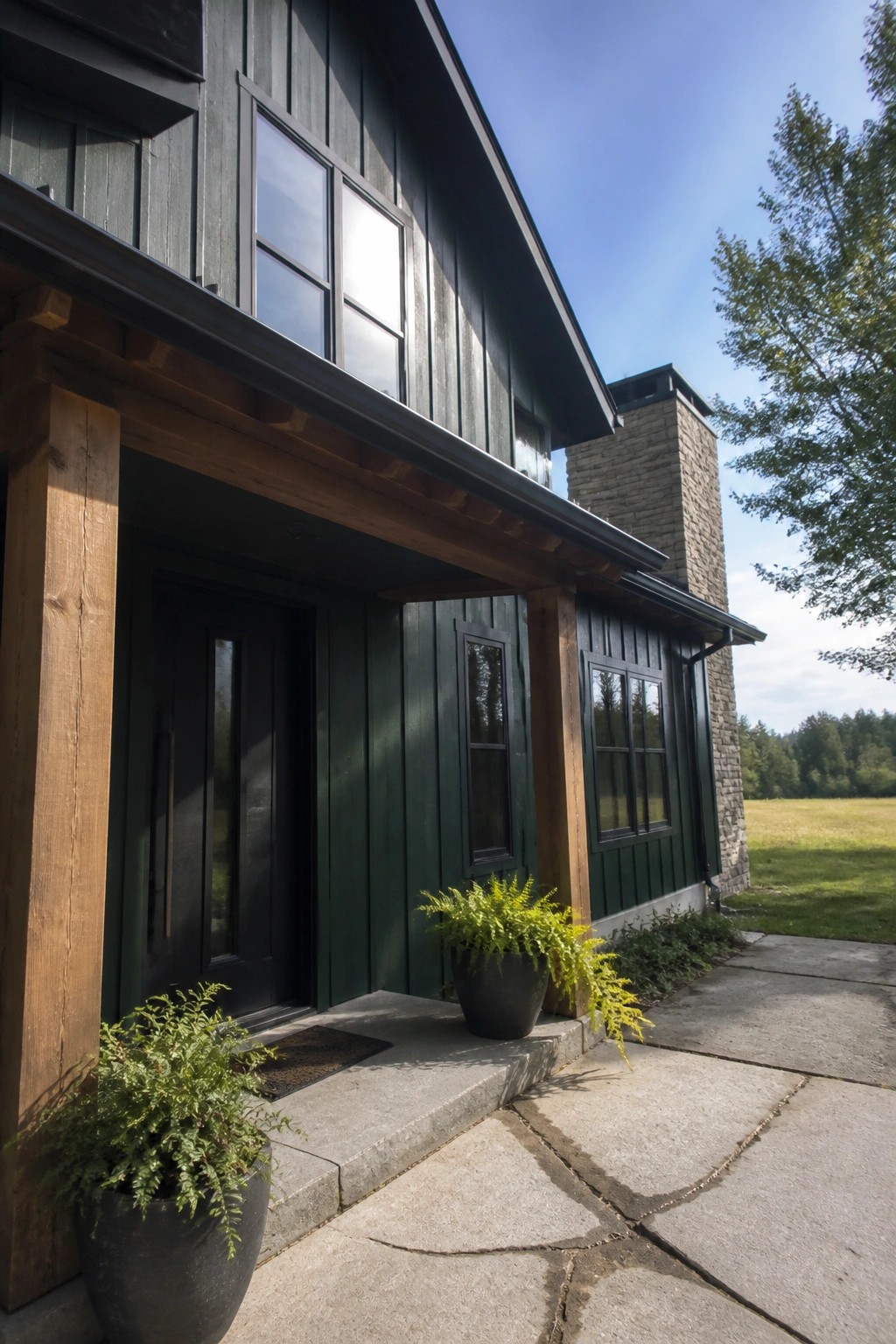 Dark green vertical siding on a rural house with wood trim and a stone chimney.