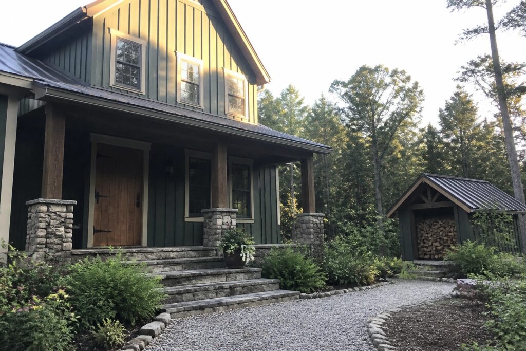 22 Striking Green Exterior Paint Colors for Wooded and Rural Homes A deep green house exterior with stone pillars and wood trim in a wooded setting.