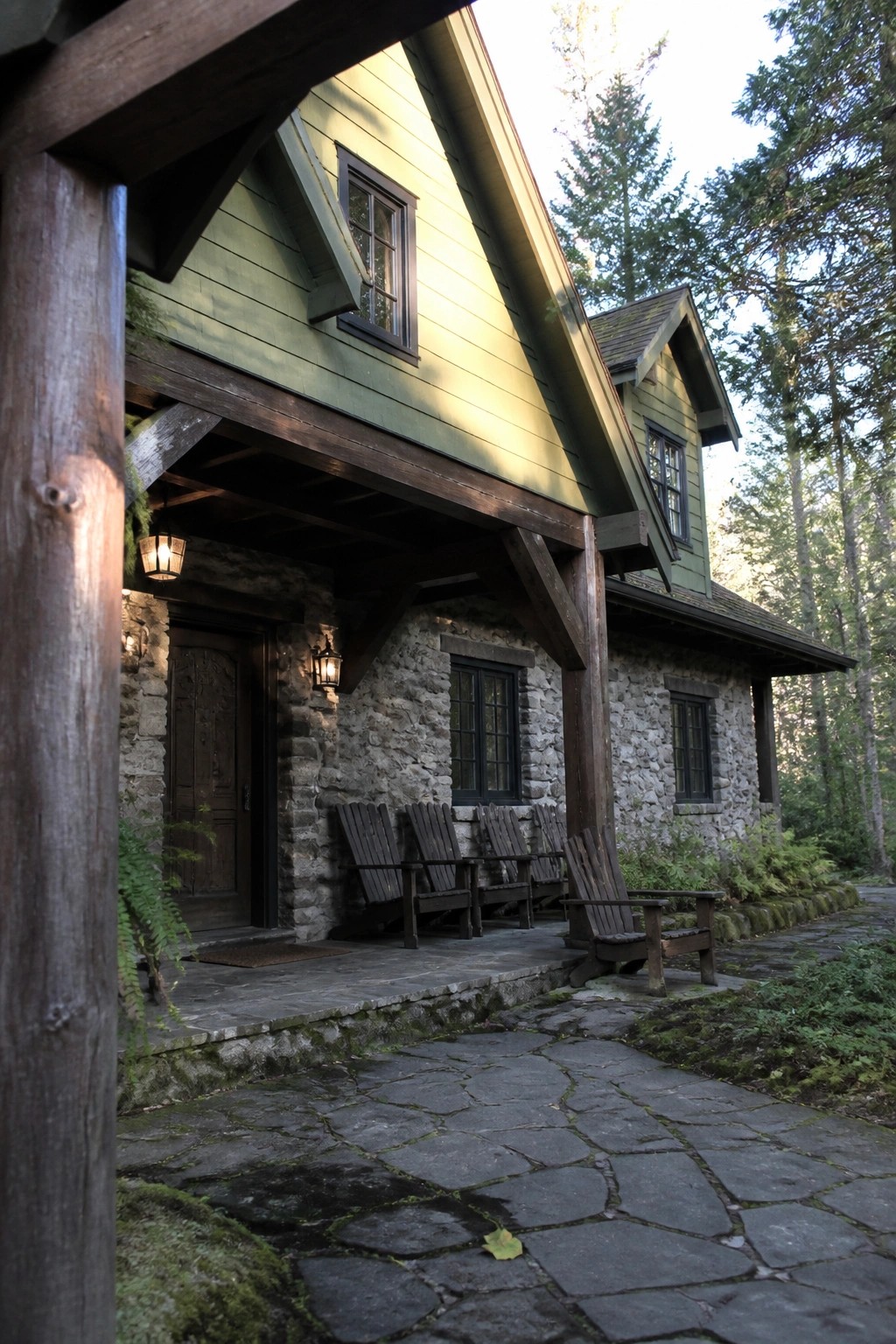 Green wooden cabin with stone walls, porch chairs, and forest stone path at dusk