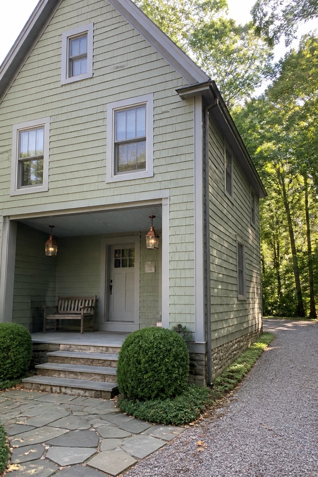 Light green shingled house with covered porch, lanterns, stone steps, and trees.