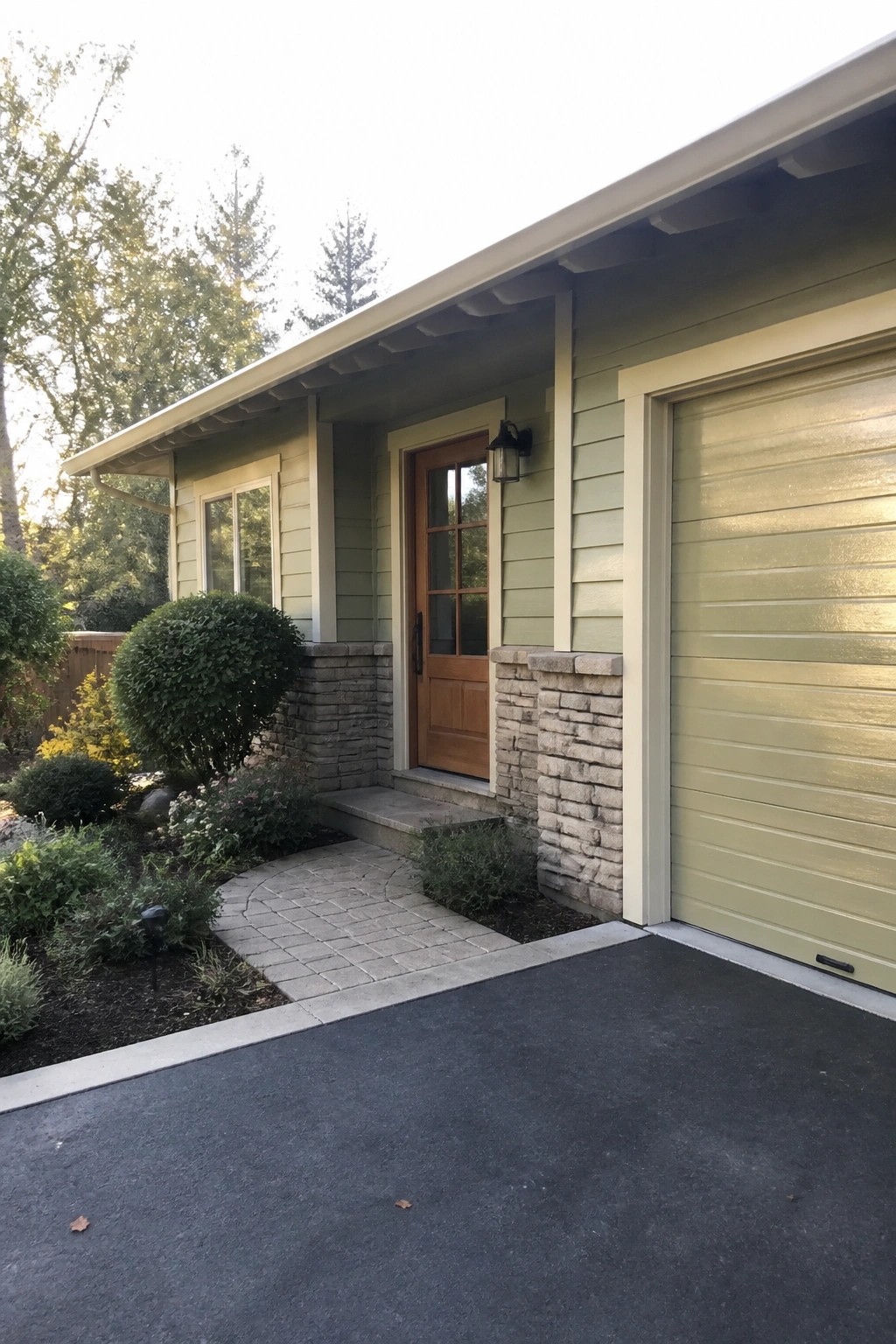 Light green house with wooden door, matching garage, stone accents and paved walkway.