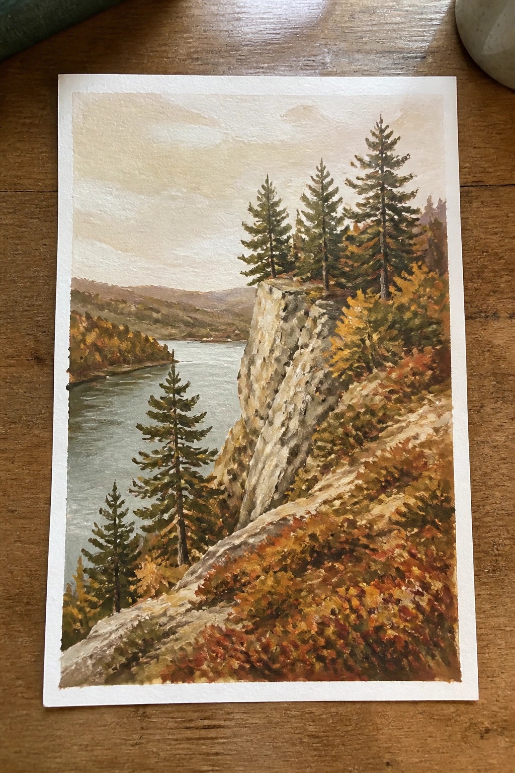Rocky cliff with pines and autumn foliage overlooking winding river in watercolor.