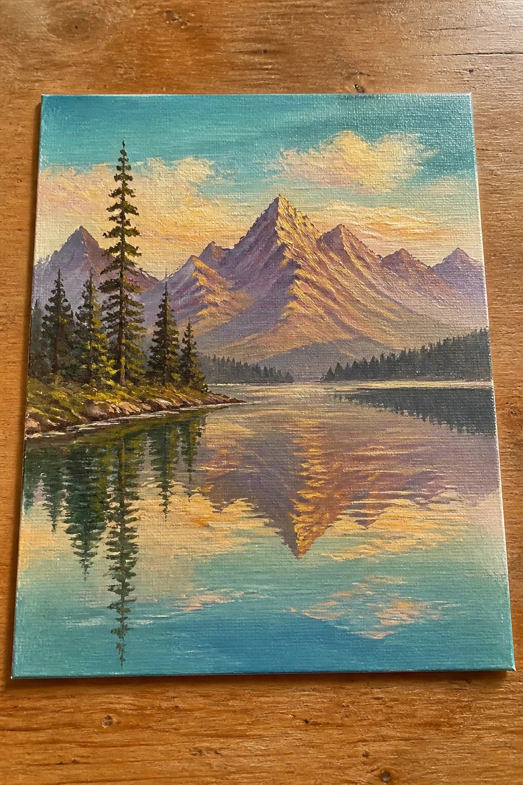 Sunlit mountain peaks reflected in a calm turquoise lake with pine trees.