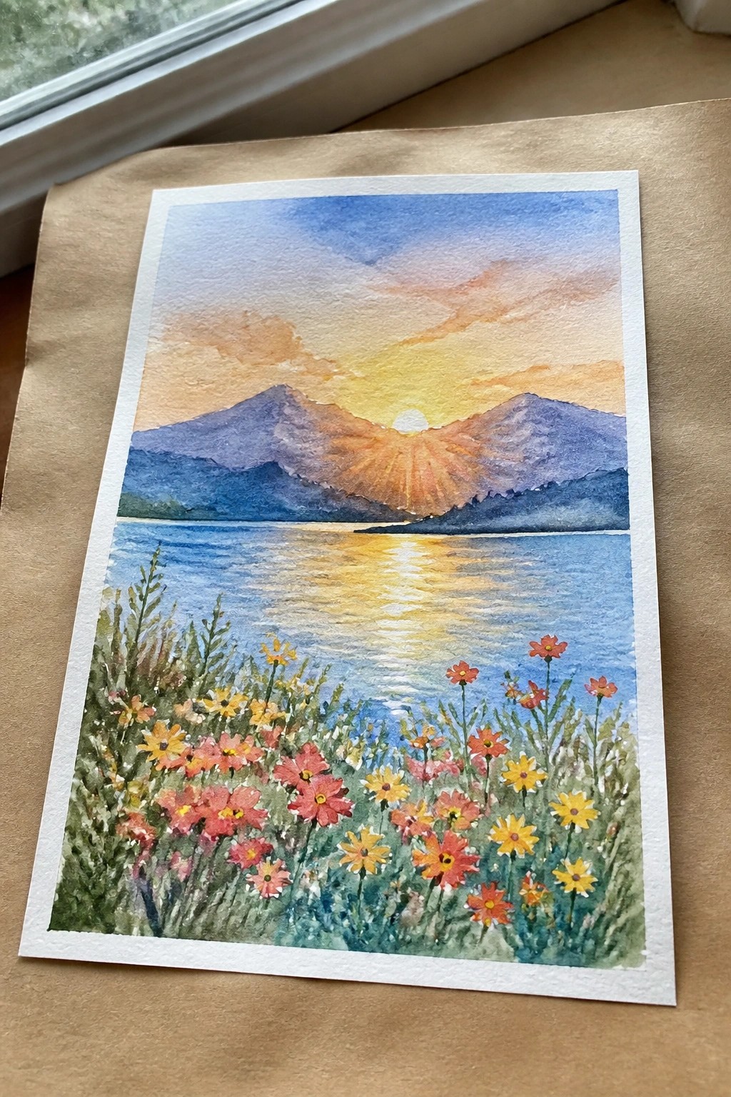 Watercolor sunset over blue mountains with golden lake reflection and pink yellow wildflowers foreground