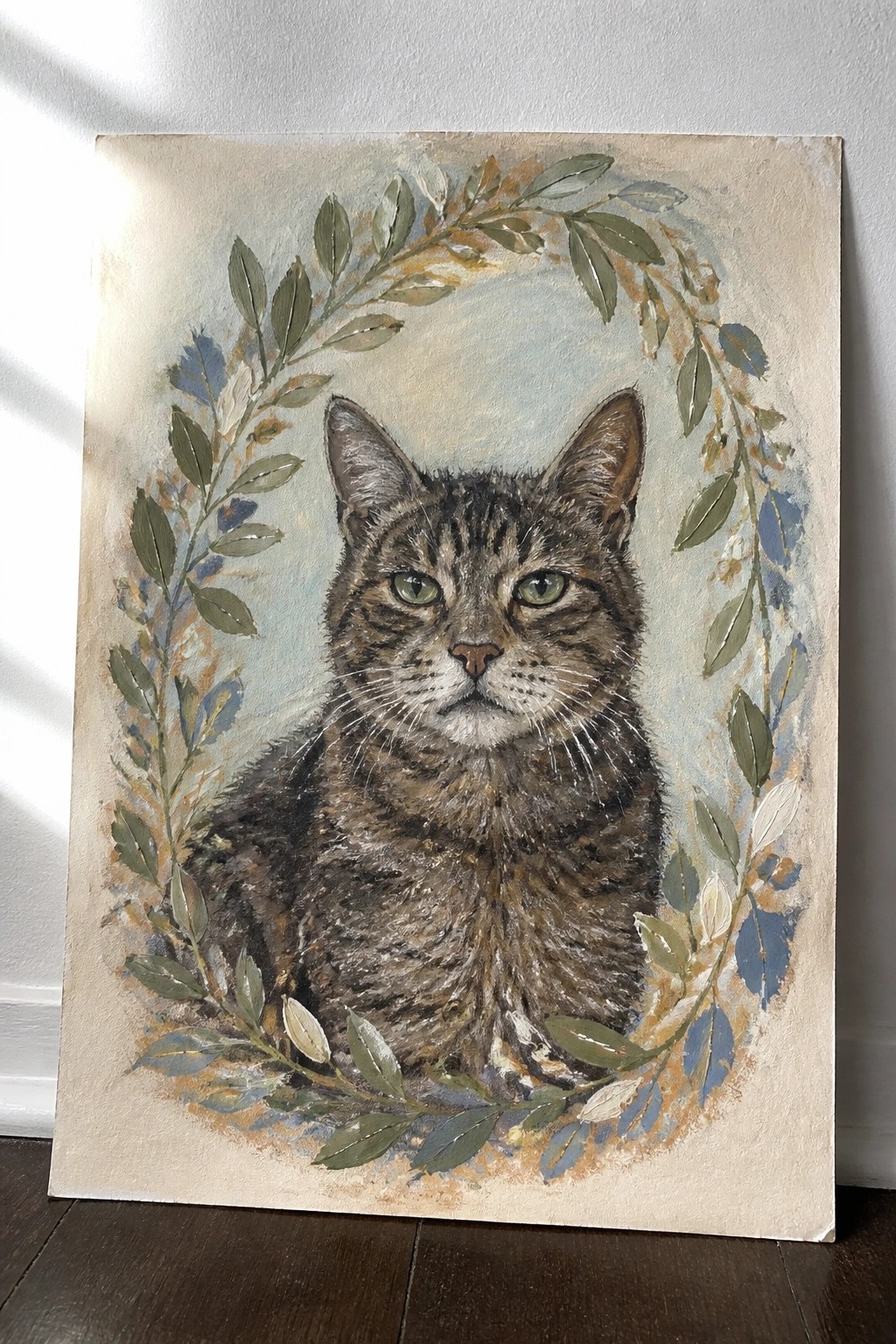 Tabby cat with green eyes centered in a circular wreath of green leaves and flowers