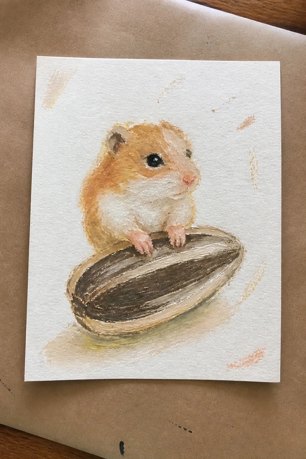 Watercolor of orange hamster perched on large striped sunflower seed