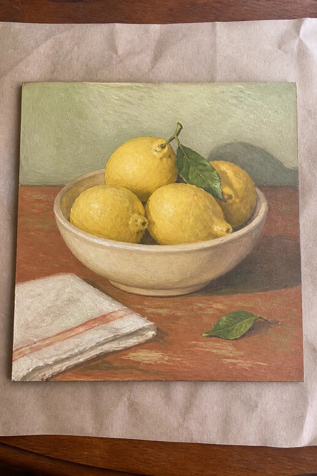Yellow lemons in white bowl on wooden table beside striped cloth and leaf