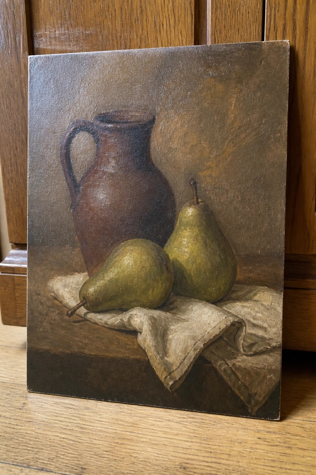 Still life painting with brown ceramic pitcher, two pears, and white cloth on wood.