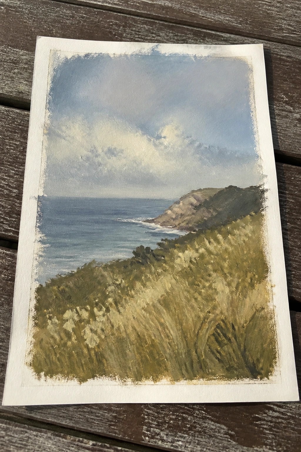 Watercolor painting of blue ocean, grassy hills, and cliffs under cloudy sky