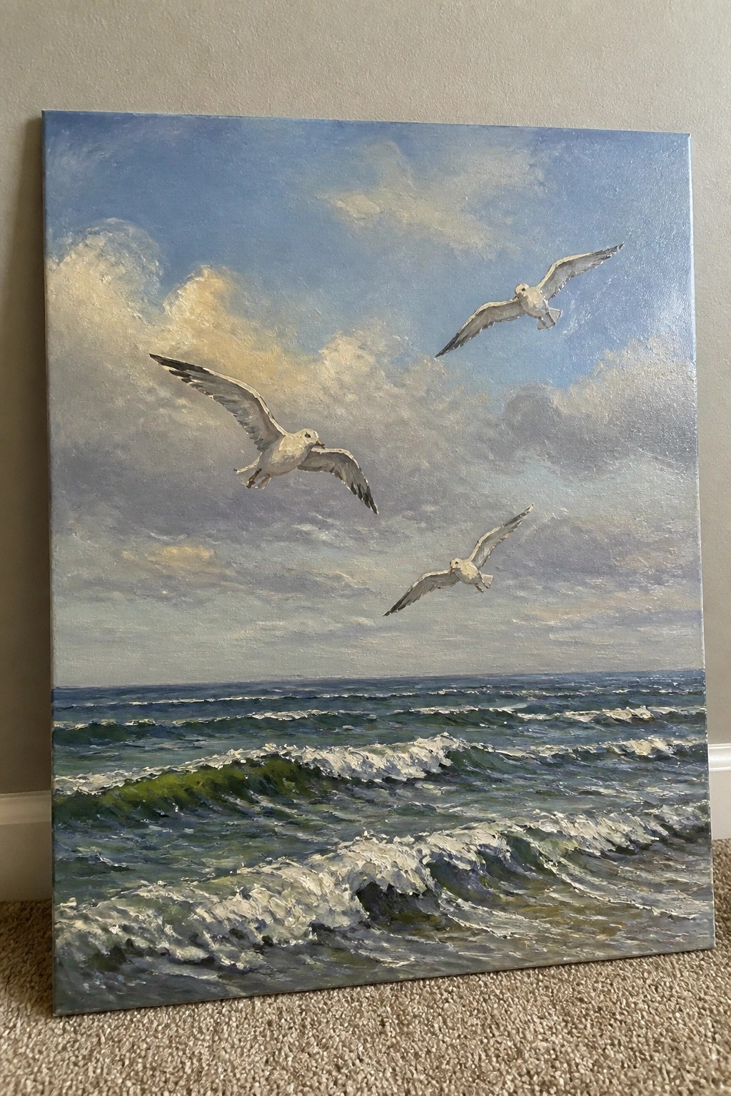 Three seagulls soaring over foamy green waves beneath a cloudy blue sky.