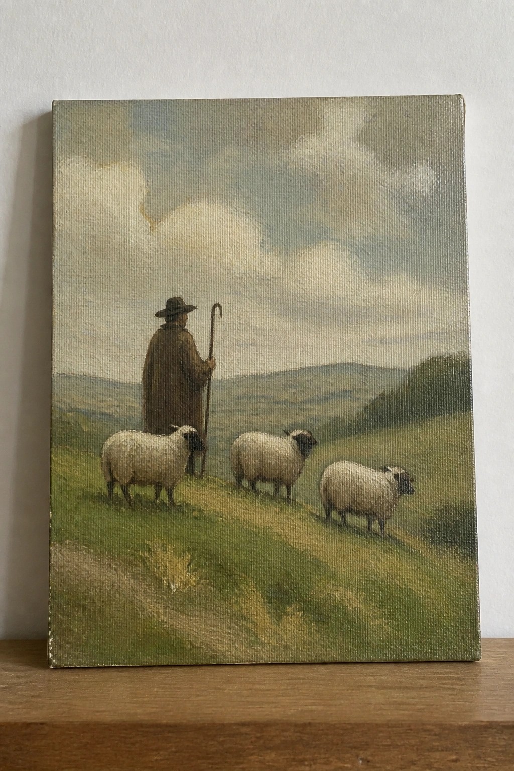 Shepherd in brown cloak and hat with staff stands by three sheep on green hills.