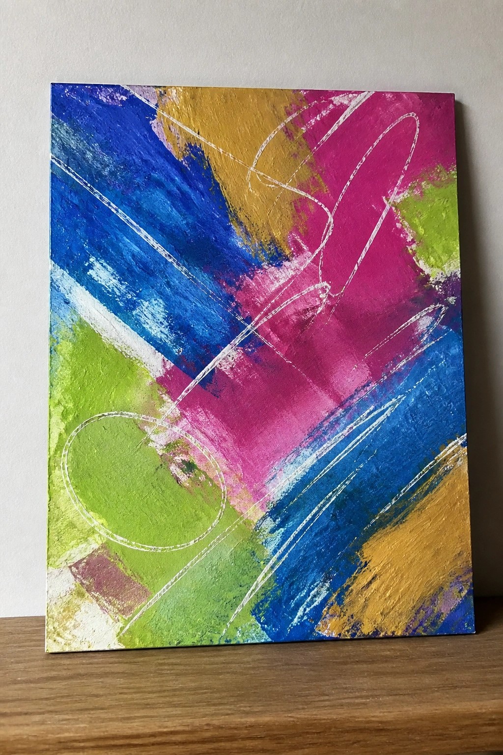Vibrant abstract canvas with bold blue, pink, yellow, green strokes and white lines on wood.