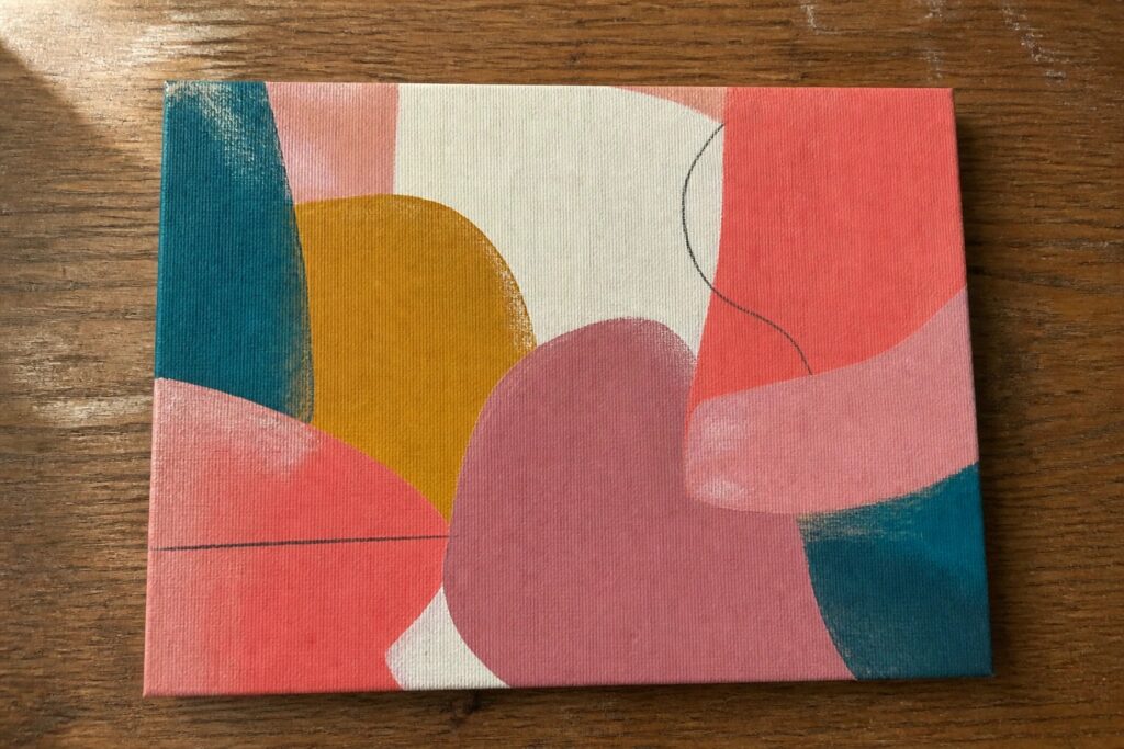 Abstract painting with teal, coral, pink, yellow shapes and dots on wood table