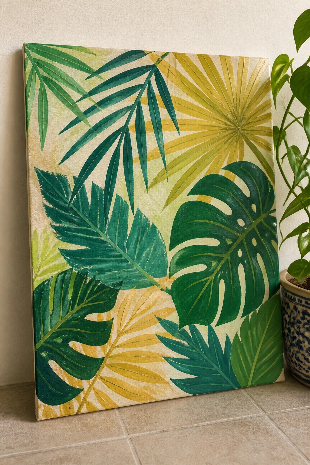 Tropical leaf painting in green and yellow on canvas beside potted plant.
