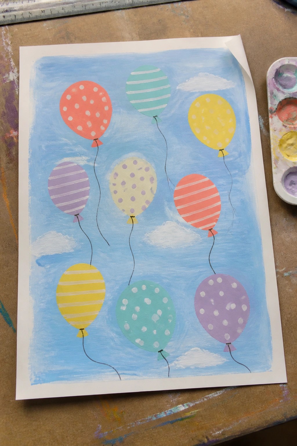 Watercolor painting of nine colorful patterned balloons floating in a blue sky with clouds