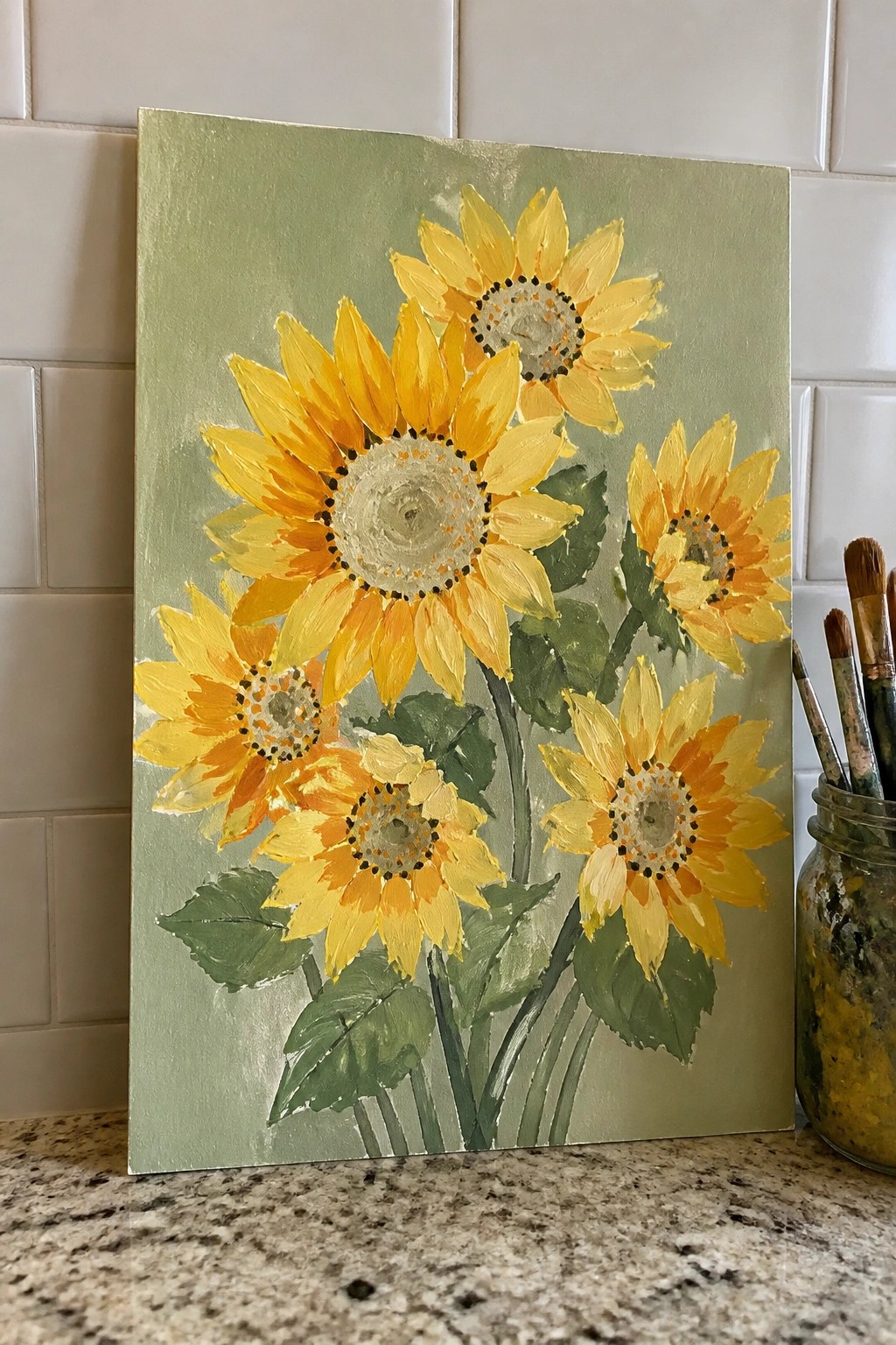 Sunflower painting on canvas with yellow blooms and green leaves beside paintbrushes