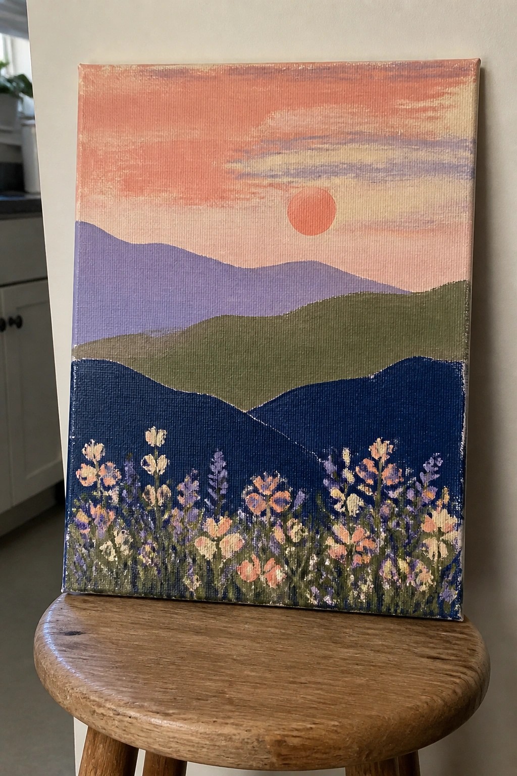 Vibrant sunset landscape painting with layered mountains and colorful wildflowers on stool