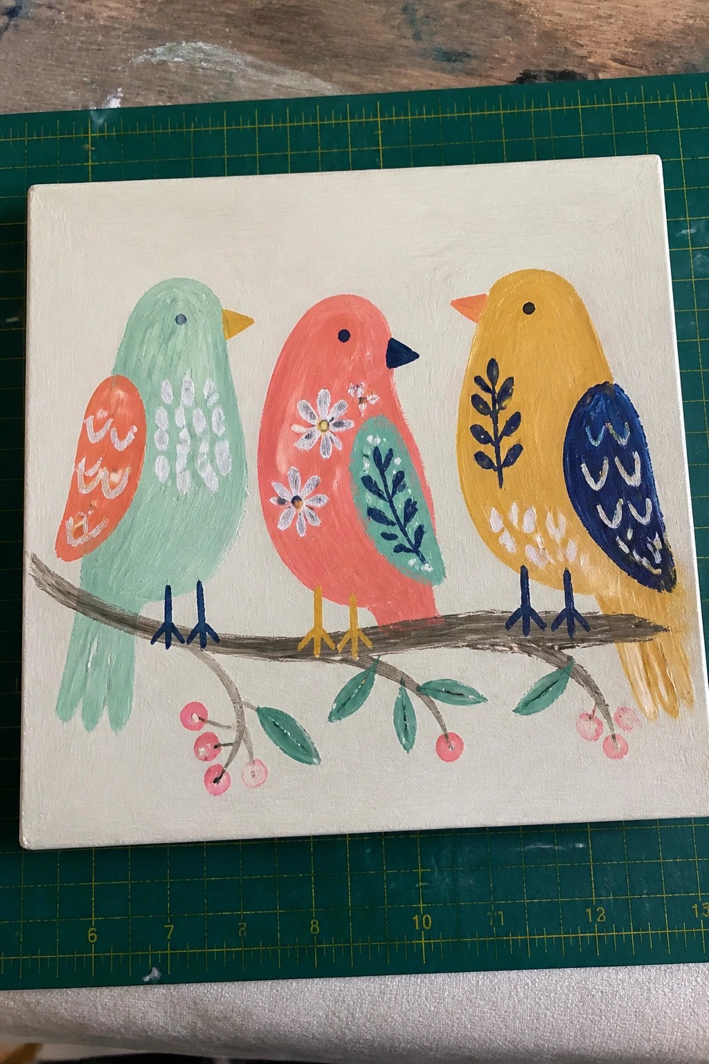 Folk art painting of three colorful birds perched on a leafy branch with berries