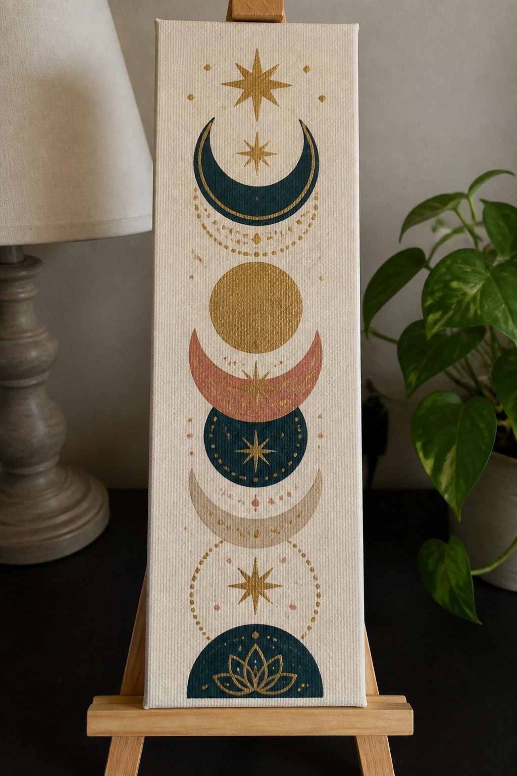 Canvas on easel displays vertical moon phases with gold stars, teal, and lotus.
