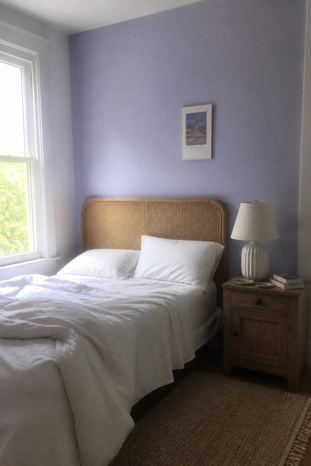Bed with white linens and rattan headboard against purple wall beside wooden nightstand