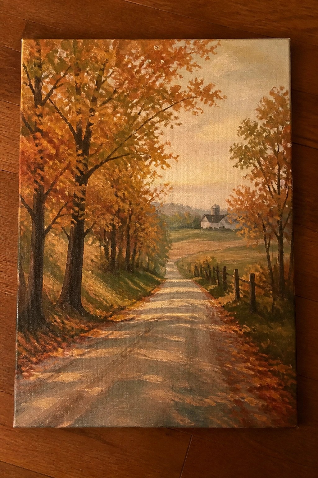 Colorful autumn trees line a leaf-strewn road leading to a distant white farmhouse and silo.