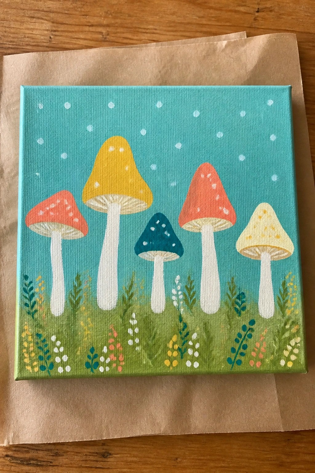Colorful mushroom painting with red, yellow, teal caps on white stems amid grass.