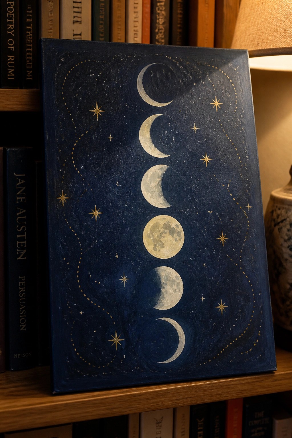Canvas with vertical moon phases in gold on deep blue among books.