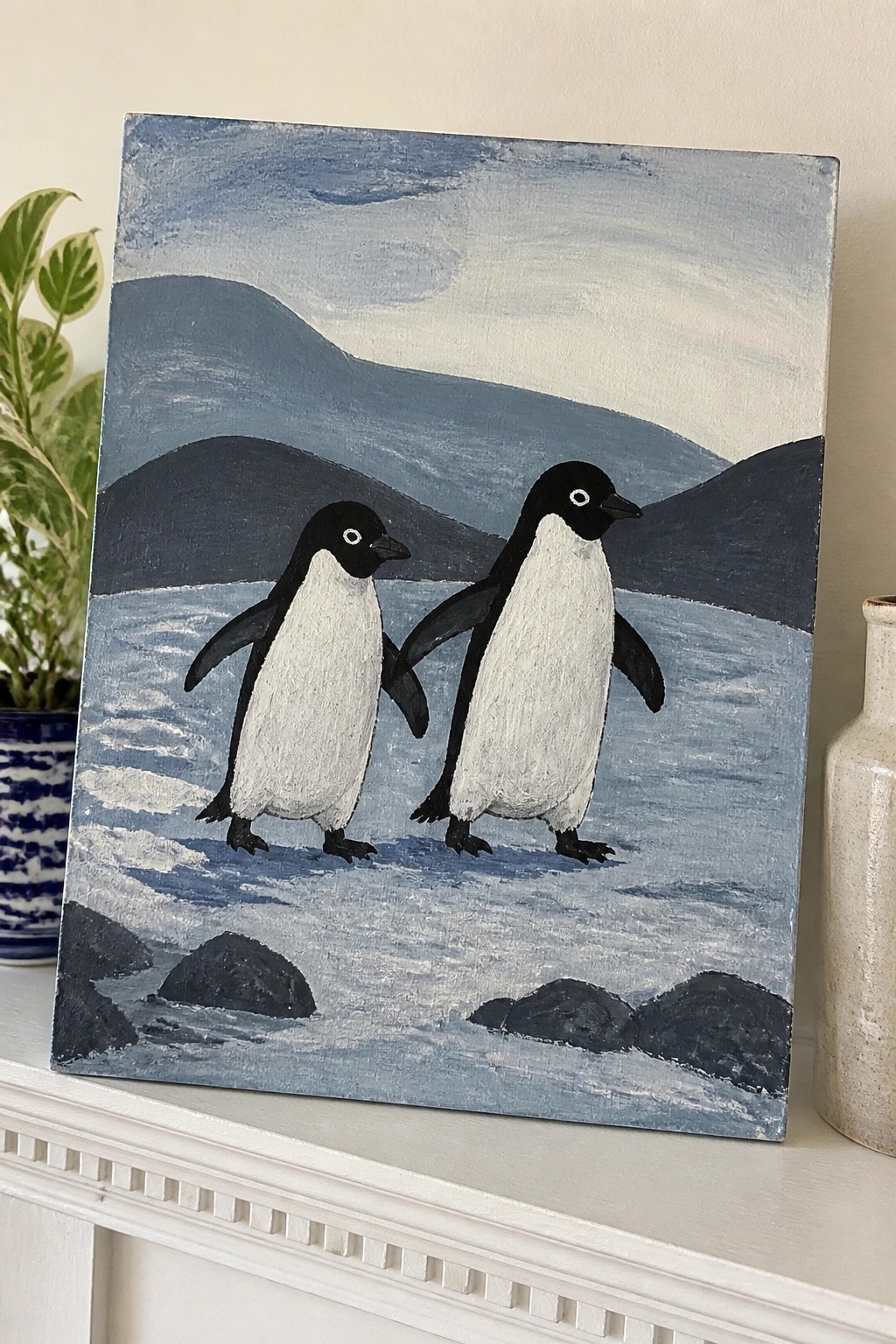 Two black-and-white penguins stand on snow before dark blue mountains and rocks.