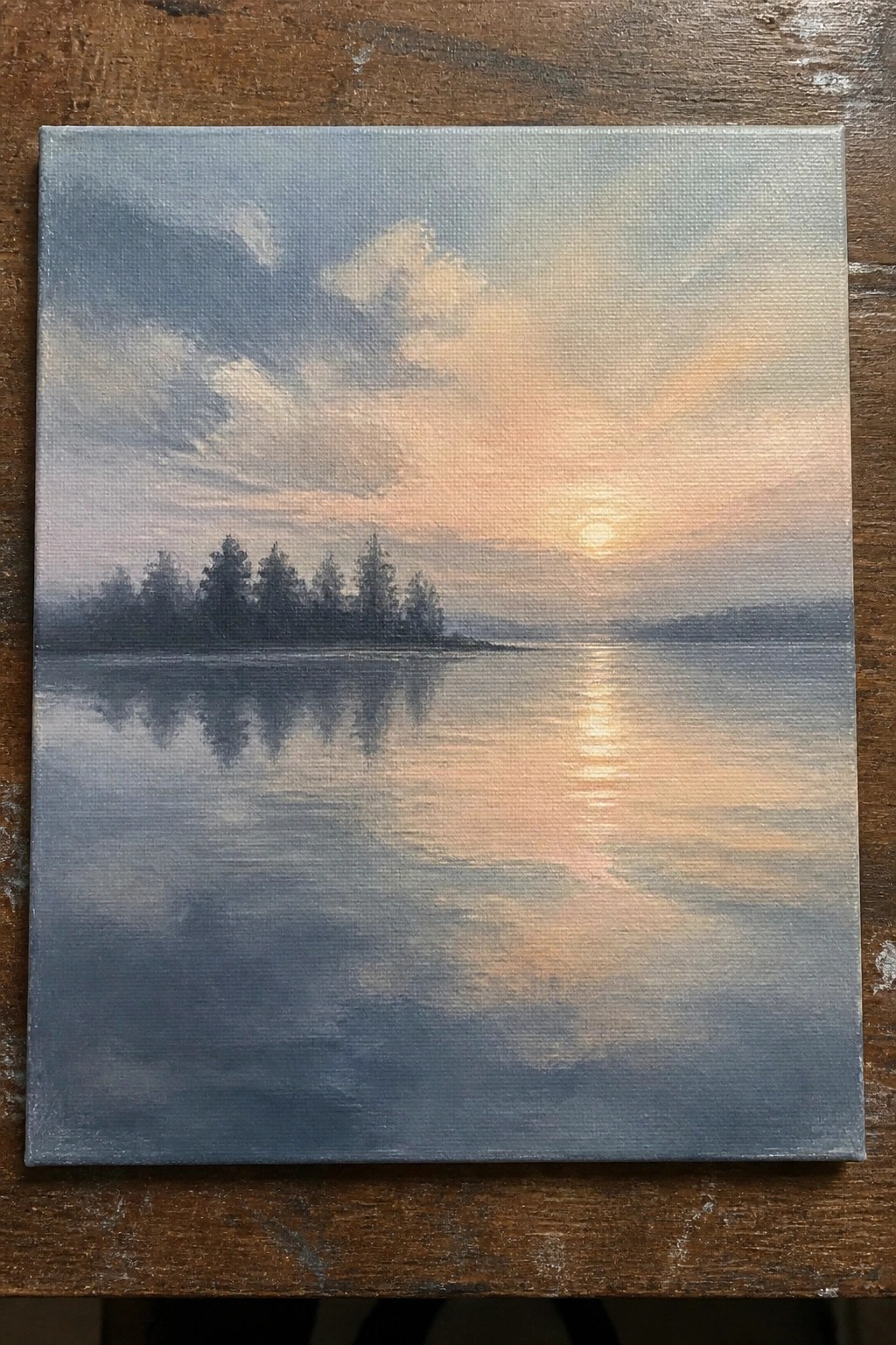A painting of a sunset over a lake with silhouetted trees on the left shore and their reflections in the water.