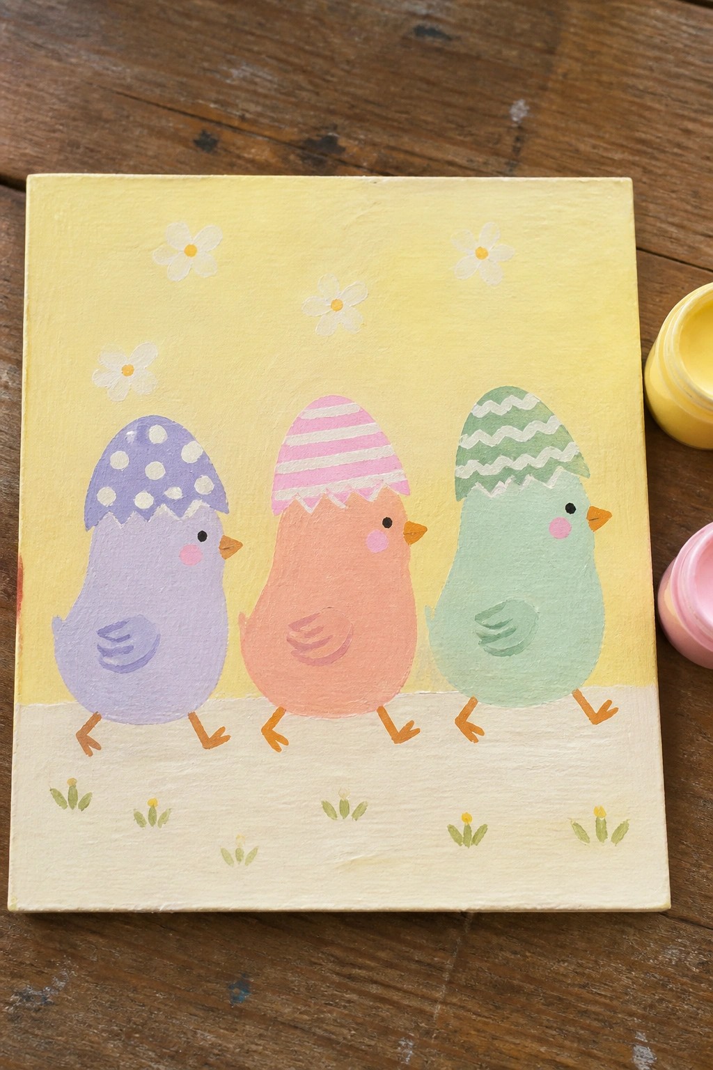 Three pastel chicks with cracked patterned eggshells on yellow canvas with flowers