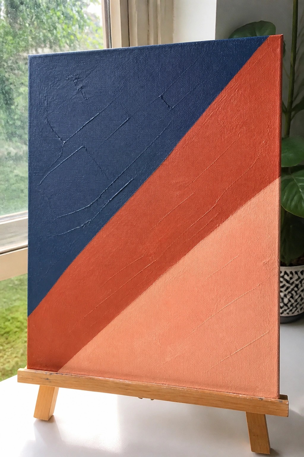 Abstract painting with dark blue, orange, and peach diagonal sections on wooden easel.