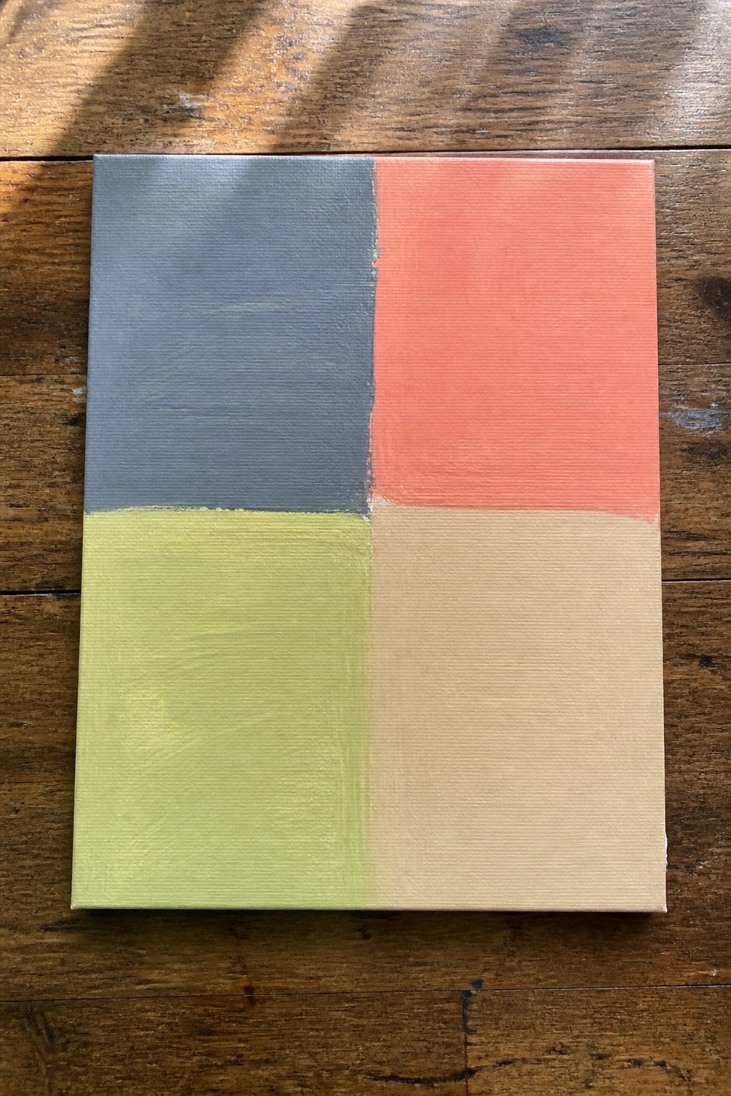 Abstract canvas with blue, coral, lime green, and beige quadrants on wood