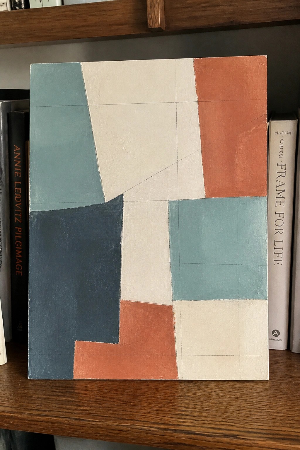 Abstract geometric painting with teal, navy, orange, and white shapes on wooden shelf