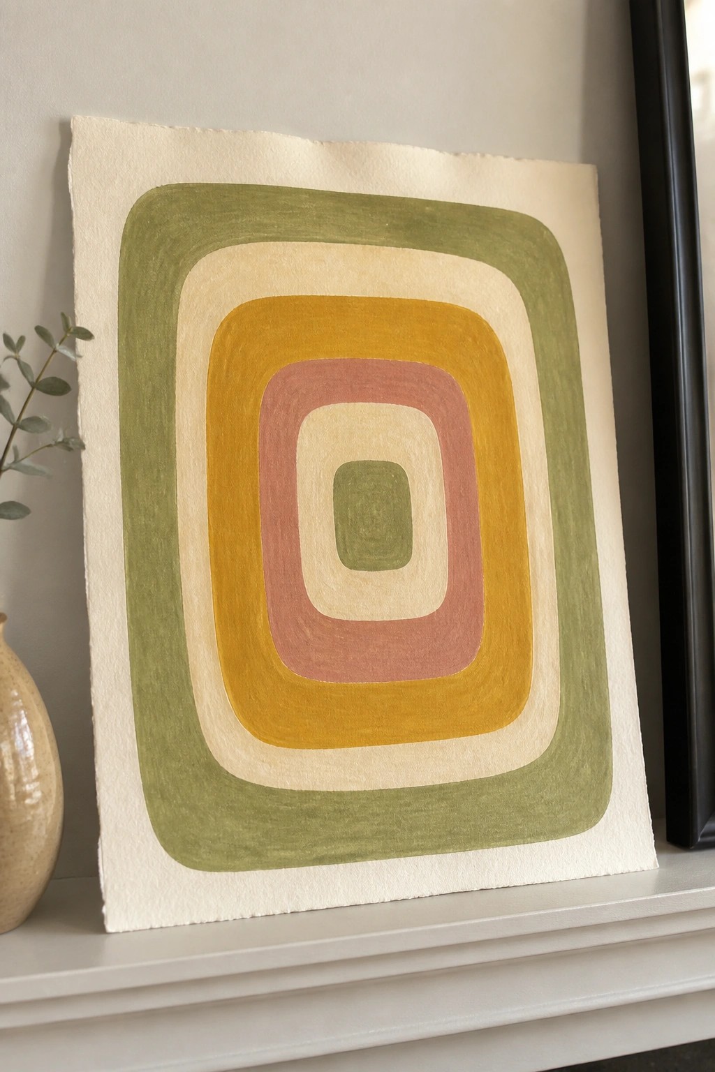Abstract concentric rounded rectangles in green, yellow, and pink on white mantel with vase.