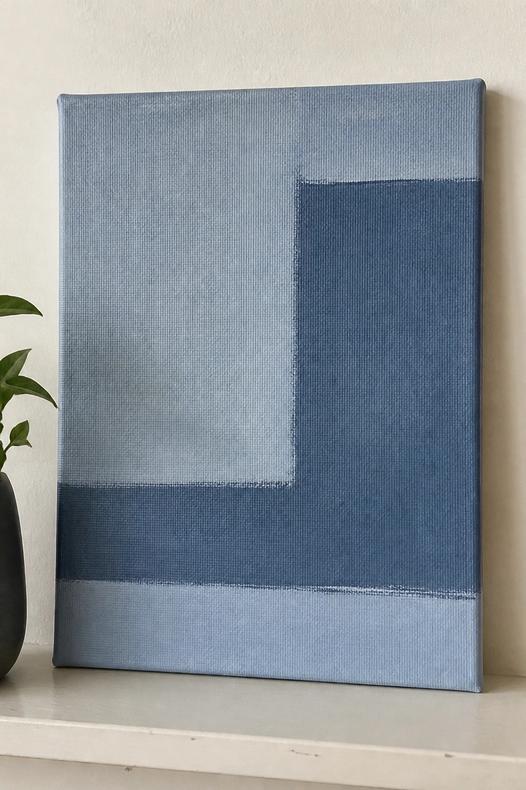 Abstract blue geometric painting on canvas beside a potted plant on a shelf.