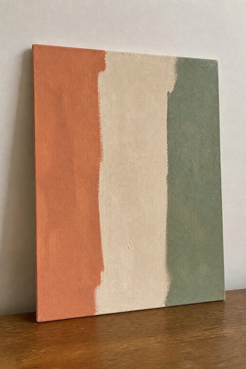 Abstract canvas with vertical orange, beige, and green stripes on wooden surface.