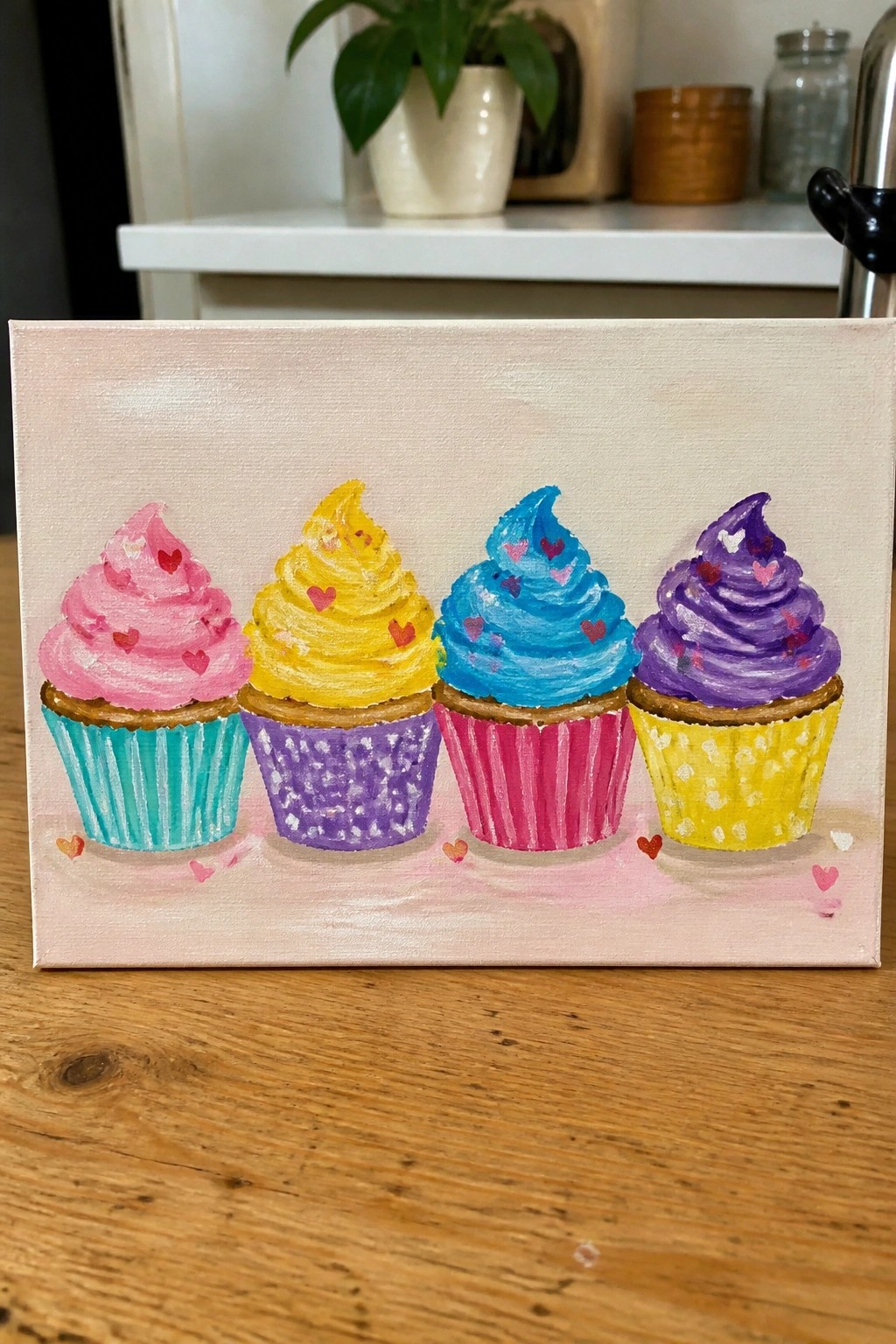 Four colorful cupcakes with pink yellow blue purple frosting and hearts on canvas