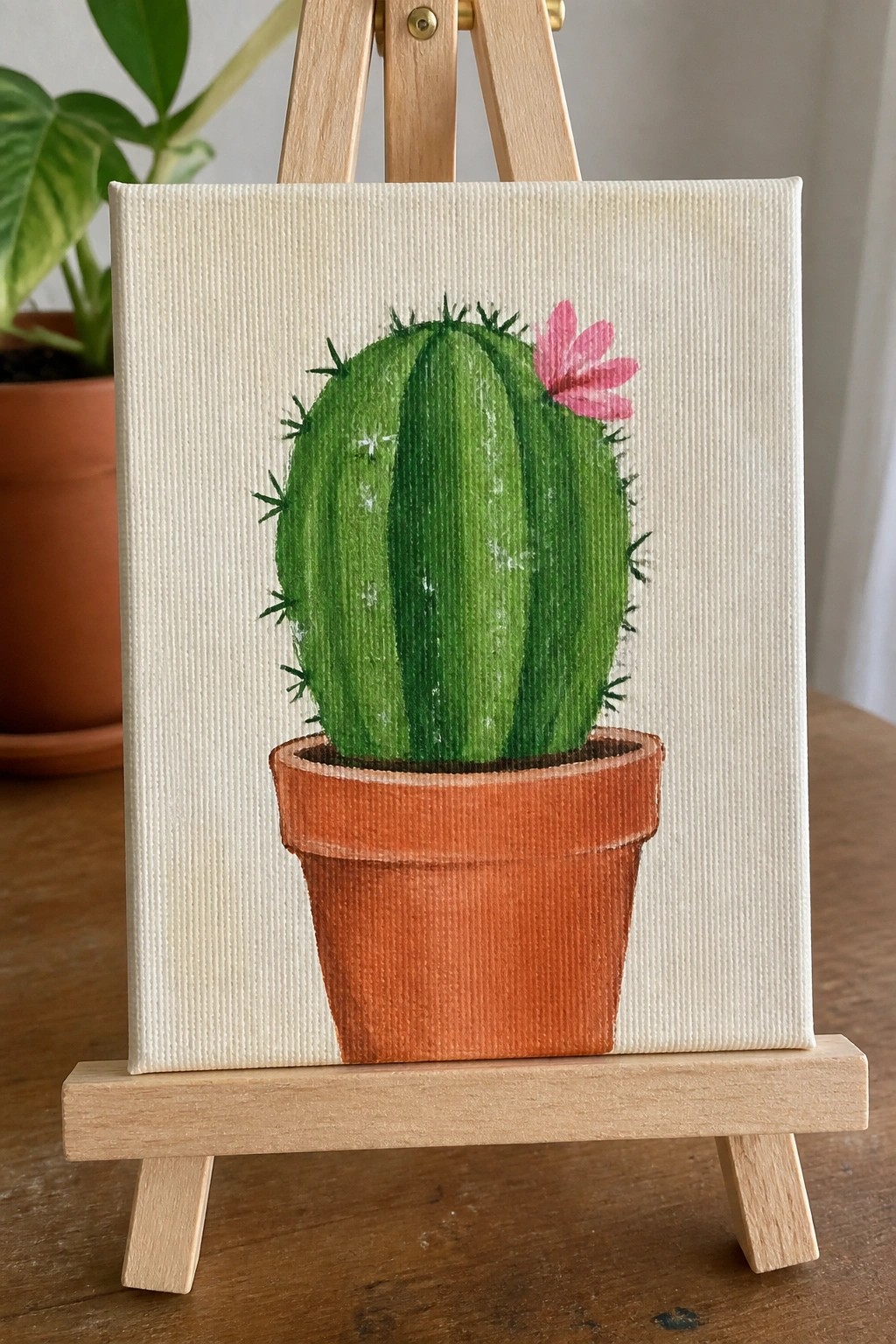 Green cactus with pink flower in terracotta pot, painted on canvas on wooden easel