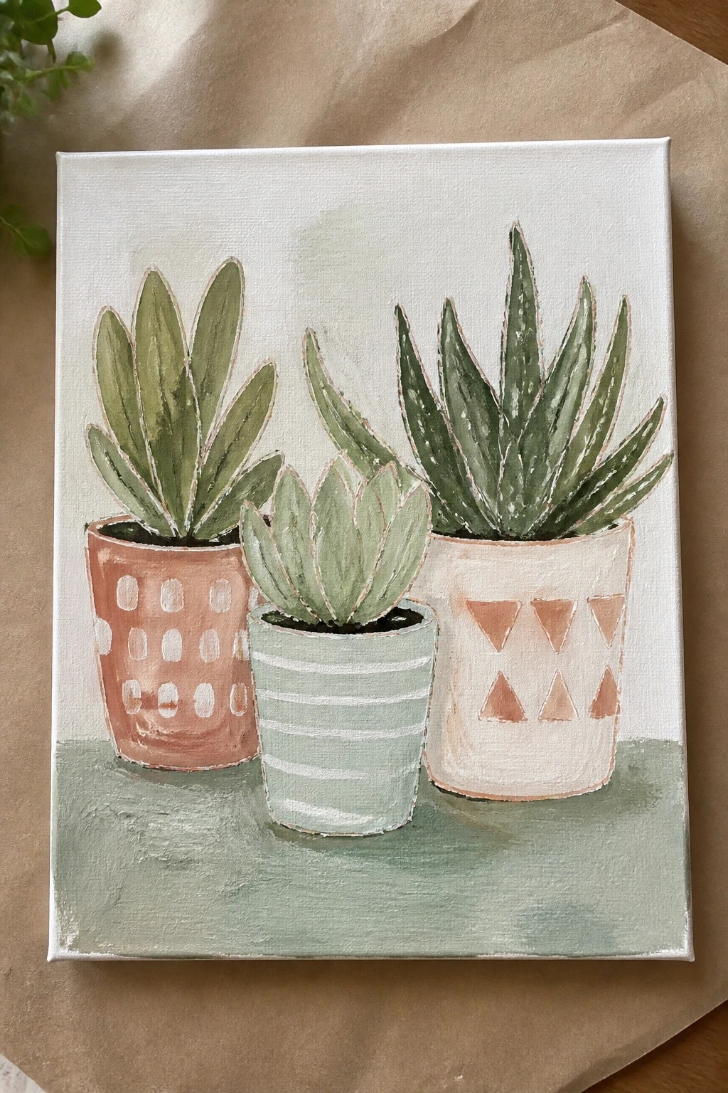 Three succulents in patterned pots on a painted canvas with green base.