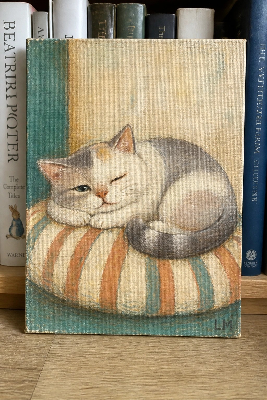 Painting of white-gray cat sleeping on orange-teal striped cushion, books behind