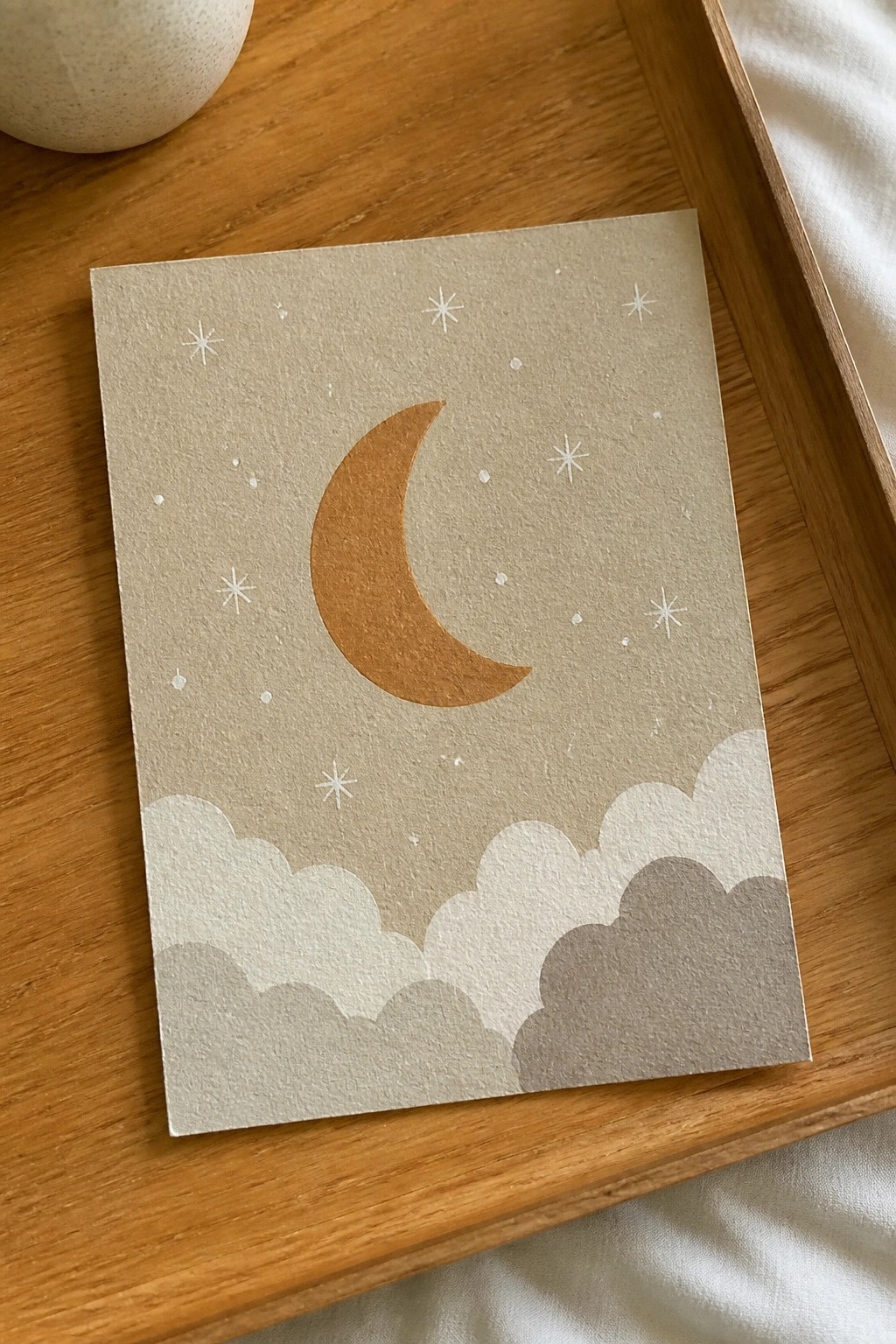 Minimalist card with terracotta crescent moon, white stars, and layered clouds on beige paper