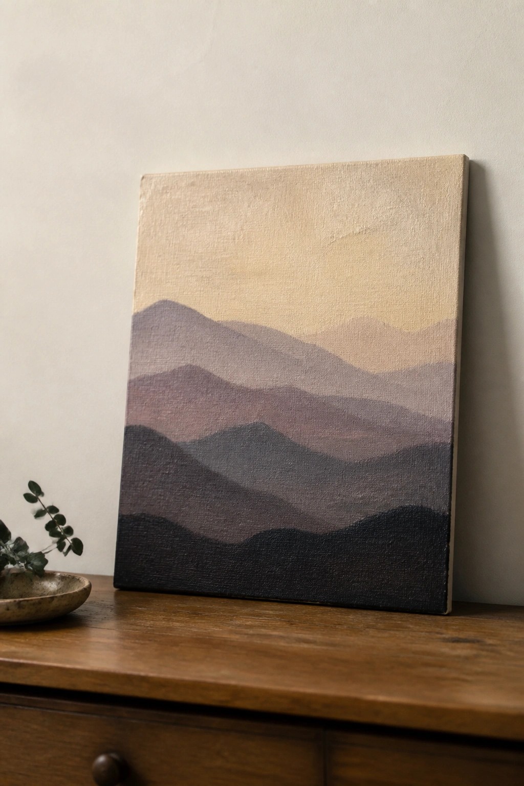 Abstract painting of layered purple mountains on canvas beside small plant bowl.