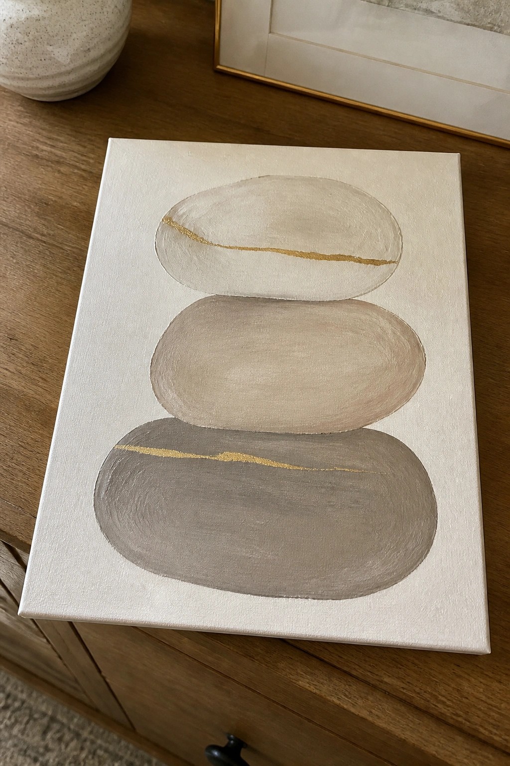 Abstract painting of three stacked neutral ovals with gold lines on canvas.