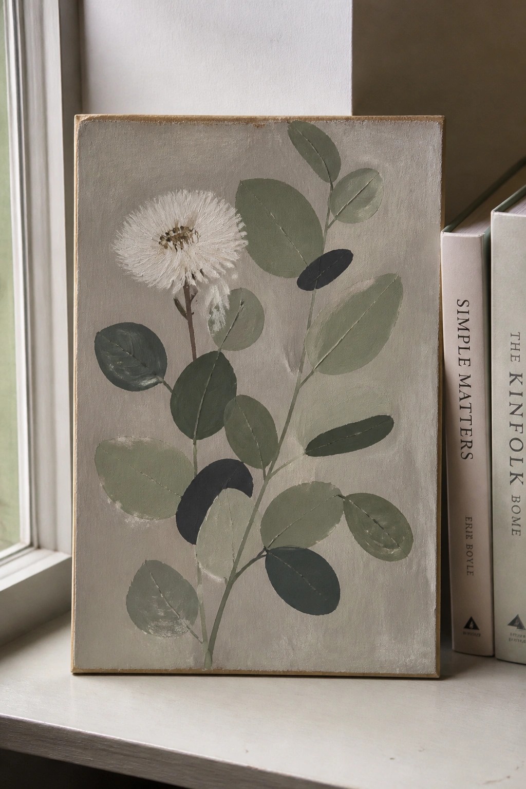 Botanical painting of white flower and green leaves beside books on windowsill